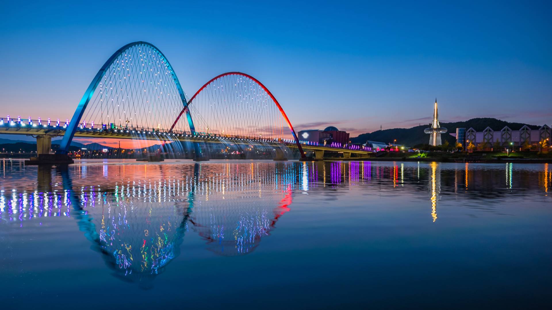 Spectacular nighttime view of Daejeon's illuminated bridge with blue and red arches reflected in calm water